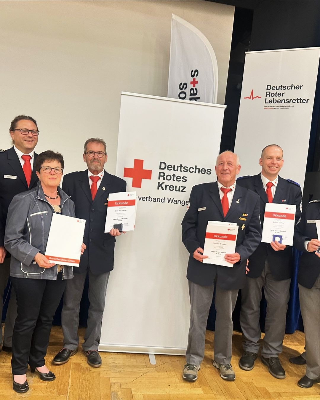 fünf Menschen halten vor einem "Deutsches Rotes Kreuz" Banner Urkunden in die Luft